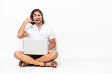 Young handsome man with a laptop sitting on the floor isolated on white background making phone gesture. Call me back sign