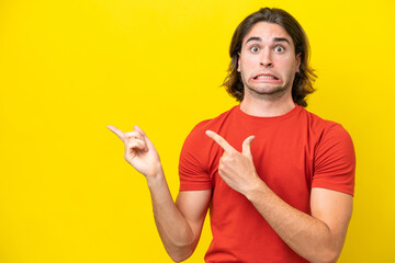 Caucasian handsome man isolated on yellow background frightened and pointing to the side