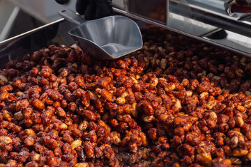 Heap of roasted caramelized sugared peanuts with warm and contrast sunlight illumination at summer outdoor food market - close up. Cookery, dessert, gastronomy and street food concept