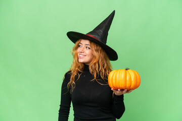 Young caucasian woman costume as witch holding a pumpkin isolated on green screen chroma key background looking side