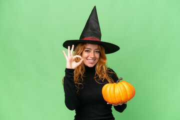 Young caucasian woman costume as witch holding a pumpkin isolated on green screen chroma key background showing ok sign with fingers