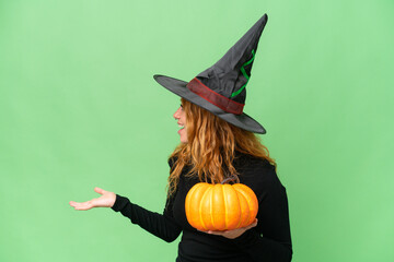 Young caucasian woman costume as witch holding a pumpkin isolated on green screen chroma key background with surprise expression while looking side