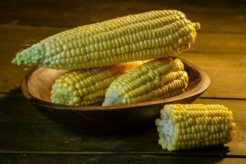 fresh raw organic ripe yellow uncooked sweet  corn cob dark rustic wooden table background closeup copy space agriculture  concept leaves plate autumn harvest banner.