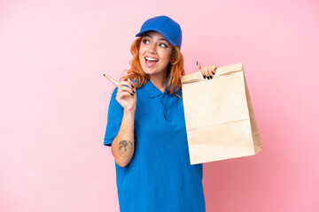 Young caucasian woman taking a bag of takeaway food isolated on pink background intending to...