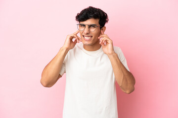 Young Argentinian man isolated on pink background frustrated and covering ears