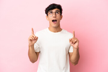 Young Argentinian man isolated on pink background surprised and pointing up