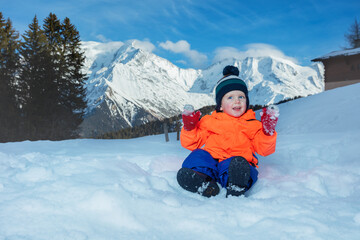 Boy in winter outfit play with snow at mountains on background