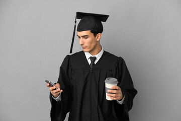 Young Argentinian university graduate isolated on grey background holding coffee to take away and a mobile