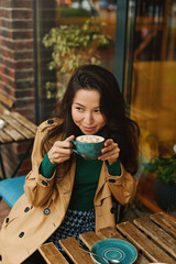 Portrait of young Asian woman drinking coffee witn apple pie in cafe on terrace of cafe. Outdoors. Cozy autumn season