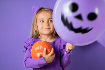 Gorgeous little girl with cat ears, balloons and a pumpkin in her hand on a purple background, Staring at the balloon monster. Halloween concept