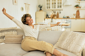 Charming young african american woman resting on sofa enjoying sunday in clean cozy living-room...