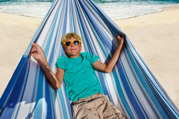 Boy with sunglasses lay in hammock on the sand beach