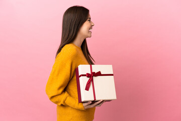 Teenager Brazilian girl holding a gift over isolated pink background laughing in lateral position