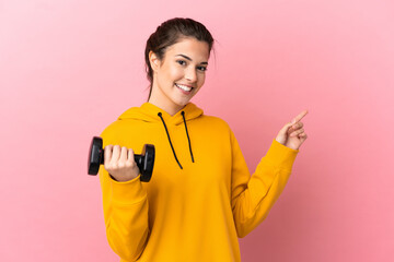 Young sport girl making weightlifting over isolated pink background pointing back