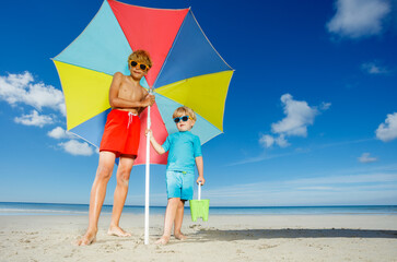 Two boys wear sunglasses stand on the beach under parasol