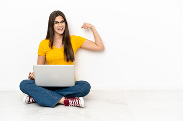 Young woman with a laptop sitting on the floor doing strong gesture