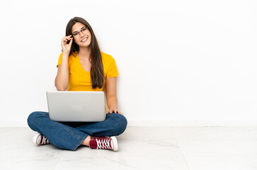 Young woman with a laptop sitting on the floor with glasses and happy