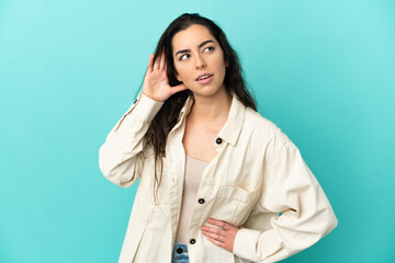 Young caucasian woman isolated on blue background listening to something by putting hand on the ear