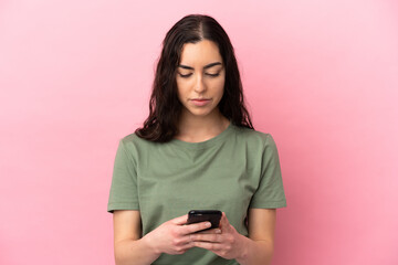 Young caucasian woman isolated on pink background using mobile phone