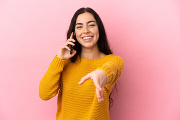 Young caucasian woman using mobile phone isolated on pink background shaking hands for closing a good deal