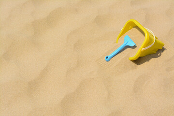 Plastic bucket and rake on sand, space for text. Beach toys