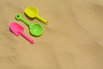 Fototapeta na wymiar Colorful plastic shovels on sand, space for text. Beach toys