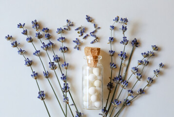 Bottle of homeopathic remedy and lavender on white background, flat lay