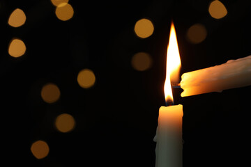 Lighting candle from another one against blurred lights in darkness, closeup. Space for text