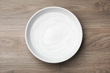 White bowl with water on wooden table, top view