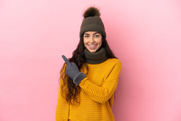 Young caucasian girl with winter hat isolated on purple background pointing to the side to present a product