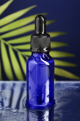 Bottle of face serum on wet surface against blue background, closeup