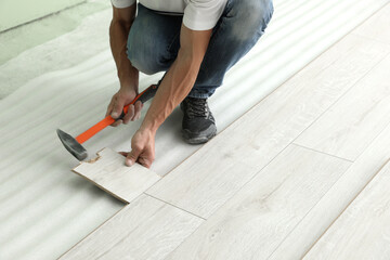 Man using hammer during installation of new laminate flooring, closeup