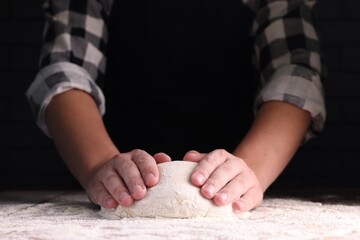 Obraz na płótnie Canvas Man kneading dough at wooden table on dark background, closeup