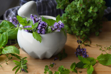Mortar with fresh lavender flowers, mint and pestle on wooden table
