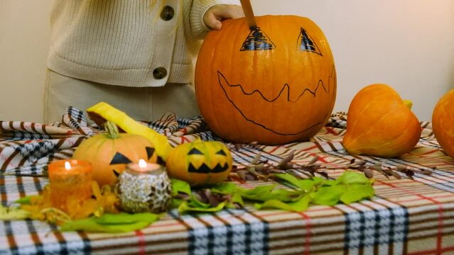 Medium plan. The girl cuts her eye on a pumpkin. Candles and small pumpkins are burning on the table. Slow motion.