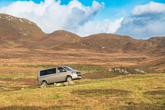Achill, IRELAND - OCTOBER 10, 2022: A VW camper T5 parking in front of a mountain face in the Irish coast. Green meadows and trees behind the automobile. No persons.