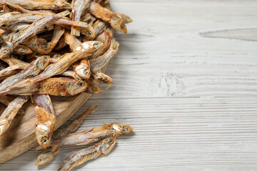 Plate of tasty dried anchovies on white wooden table, closeup. Space for text