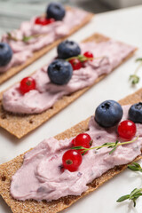 Tasty cracker sandwiches with cream cheese, blueberries, red currants and thyme on white board, closeup