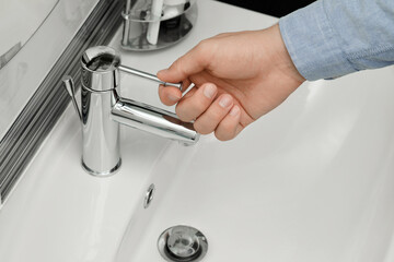 Man using water tap in bathroom, closeup