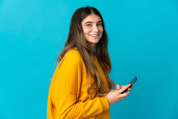 Young caucasian woman isolated on blue background sending a message or email with the mobile