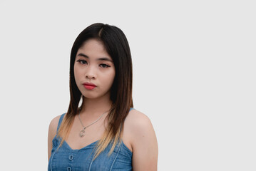 Fototapeta premium A serious Asian young woman puts on a blank expression as she looks straight at the camera for a studio shot isolated on a white background.