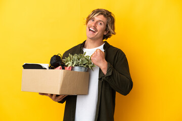 blonde man making a move while picking up a box full of things isolated on yellow background celebrating a victory