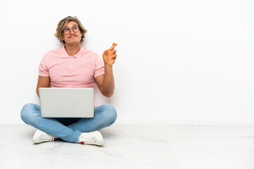 Young caucasian man sitting on the floor with his laptop isolated on white background with fingers...