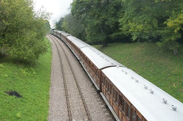 A steam train pulling victorian coaches through the English countryside.