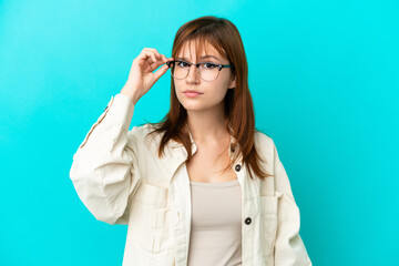 Redhead girl isolated on blue background With glasses and frustrated expression