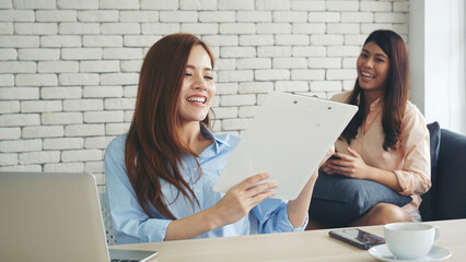 Two businesswomen team meeting using laptop at company office desk. Two young Female freelance reading financial graph charts Planning analyzing marketing data. Asian people team working office firm.
