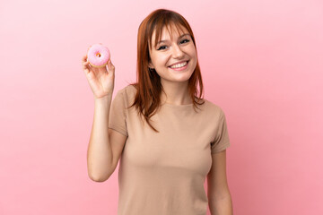 Redhead girl isolated on pink background holding a donut and happy