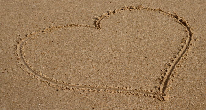 A love heart drawn in the sand of a beach in France. The texture of the sand is visible.