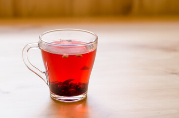 Red berry tea in a transparent cup on the background of a wooden table in a cafe