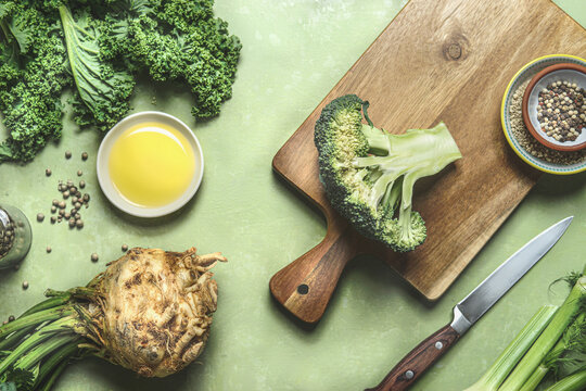 Healthy vegetarian cooking with green vegetables. Broccoli on cutting board with knife on kitchen table with olive oil, fennel , selery and kale. Top view